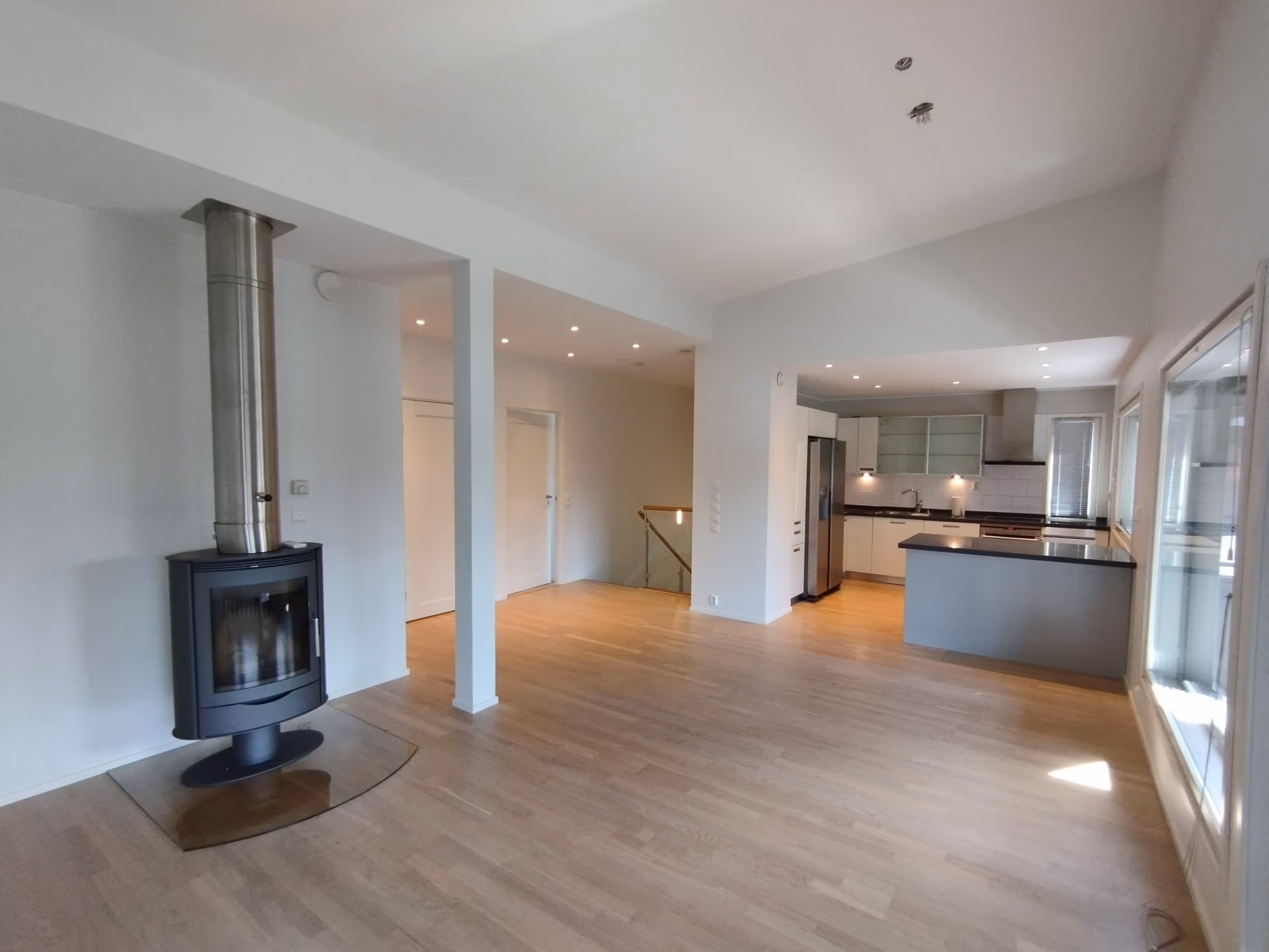 Valoisa ja avara huone, jossa on puulattia, takka ja keittiö.