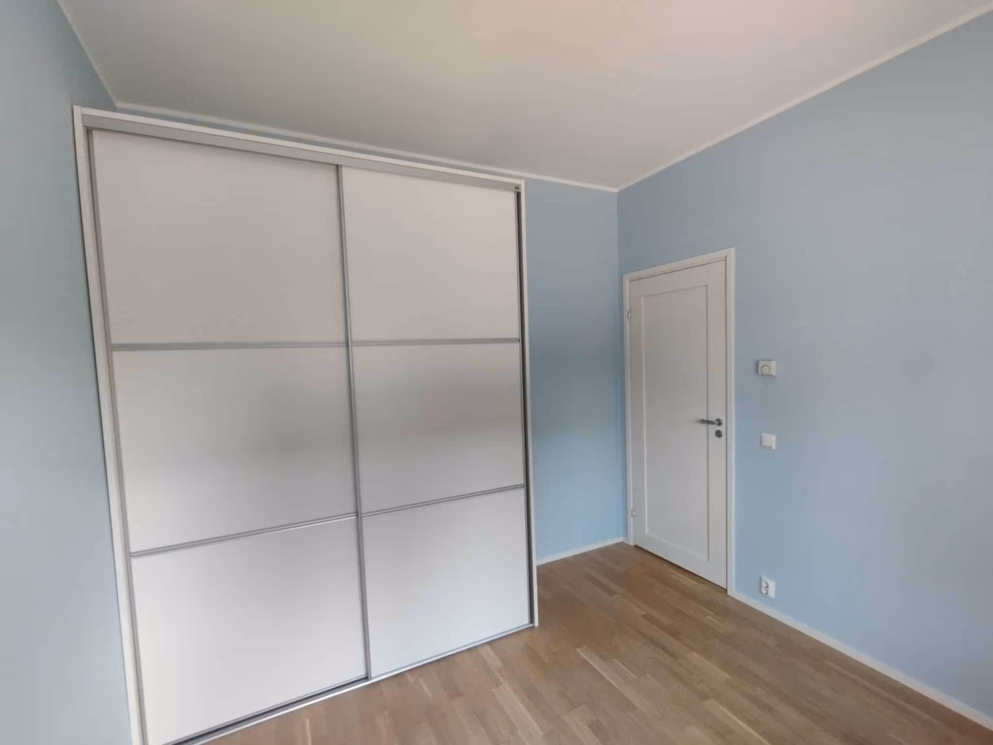 Vaaleansininen huone, jossa on valkoinen vaatekaappi, valkoinen ovi ja puulattia.