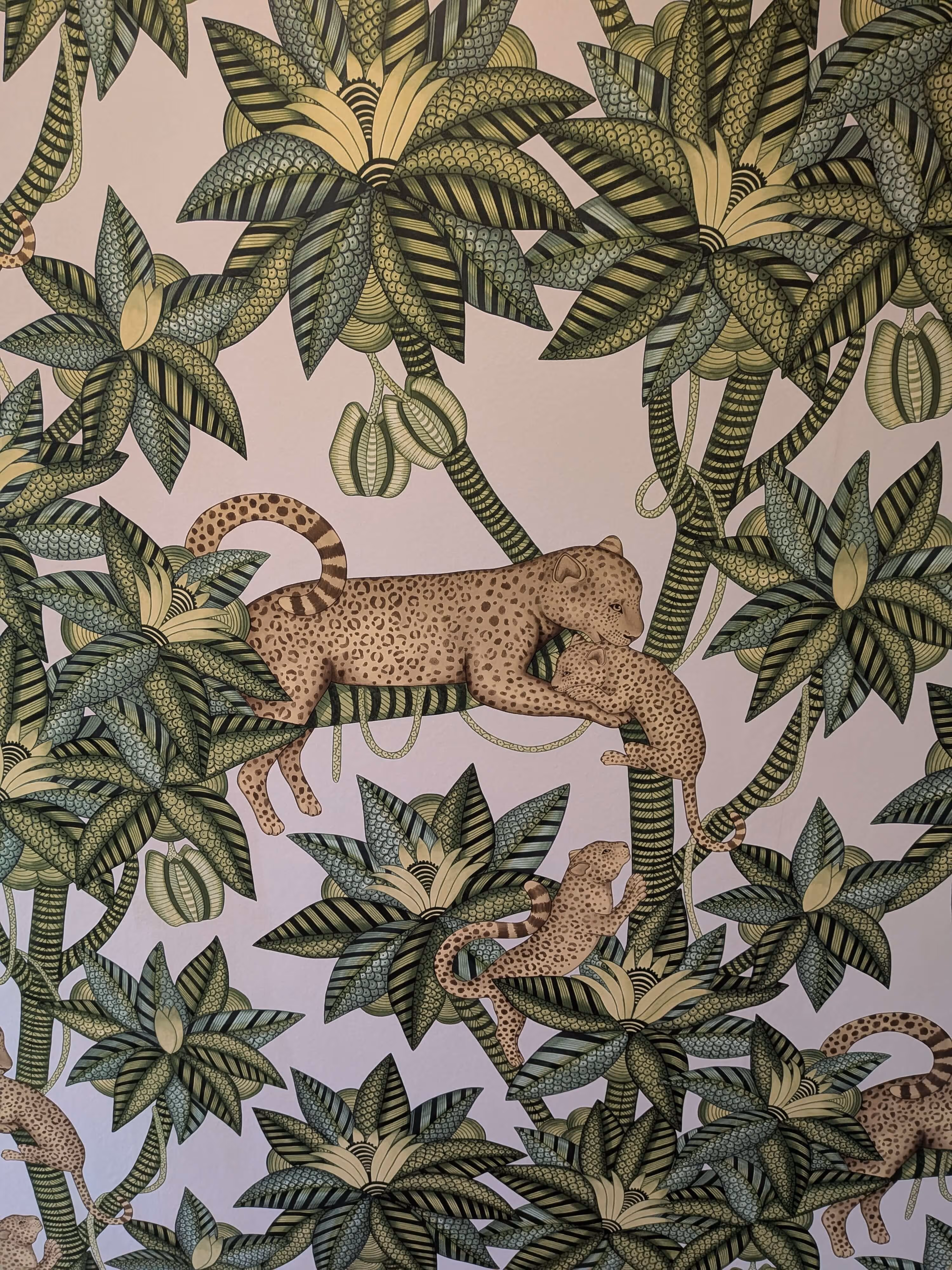 Kuvassa on tyylitelty, värikäs tapetti, jossa on leopardeja ja trooppisia kasveja vaalealla taustalla. Kasvit ovat pääosin vihreitä ja keltaisia, ja niissä on koristeellisia kuvioita. Leopardit ovat ruskeita ja niissä on täpliä.