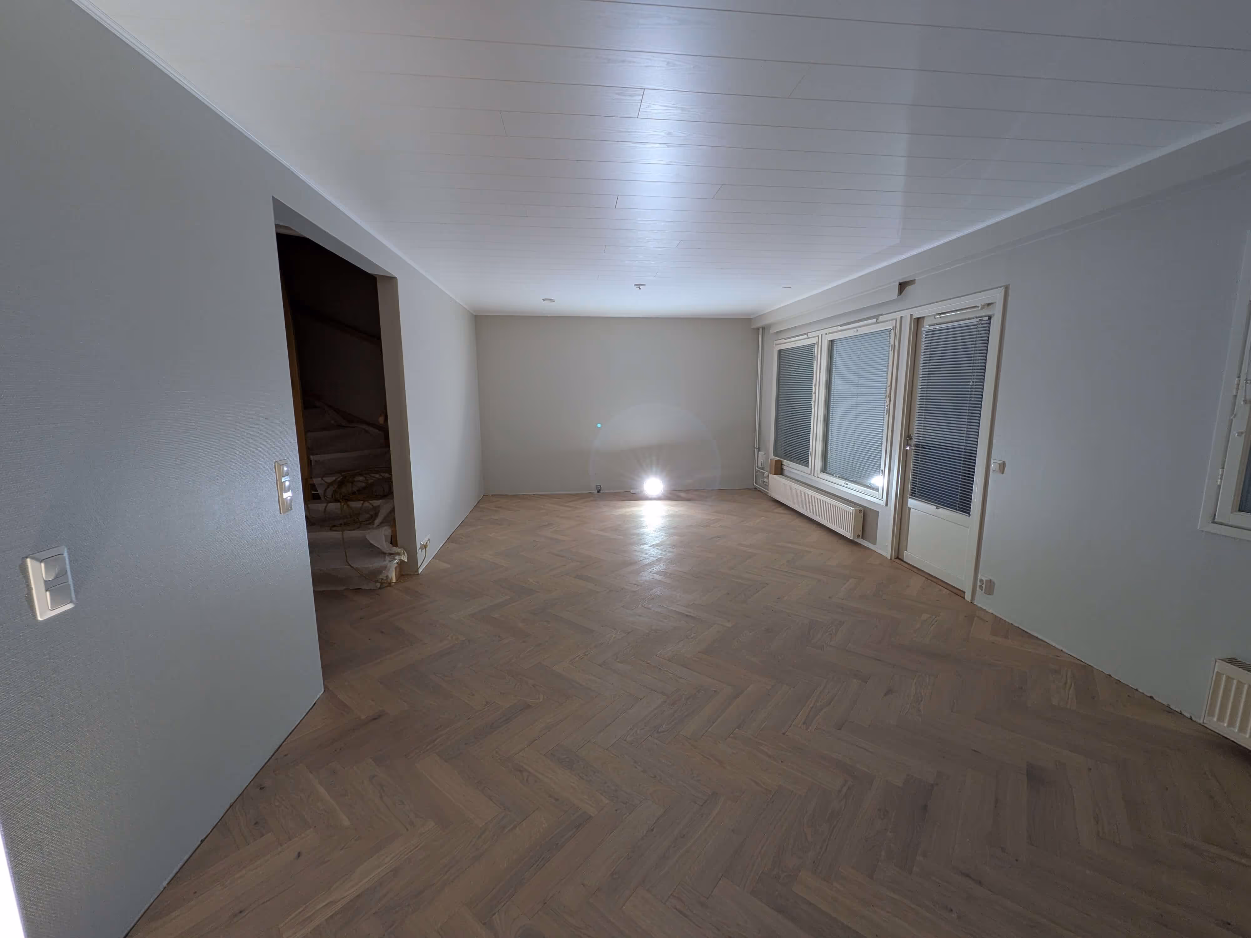 Tyhjä huone, parkettilattia, valkoiset seinät.